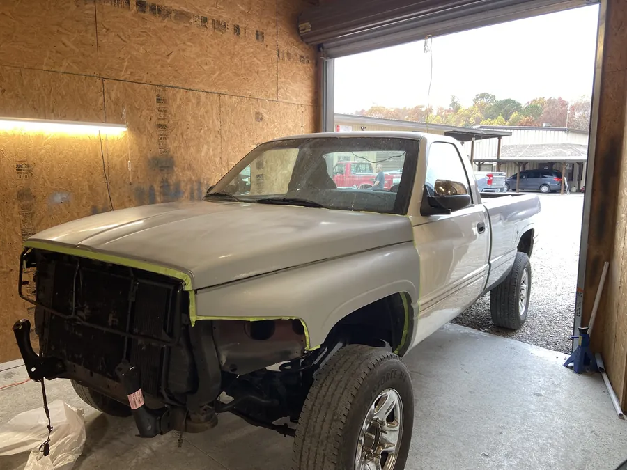 A white pickup in the shop bay with its front end masked for paint